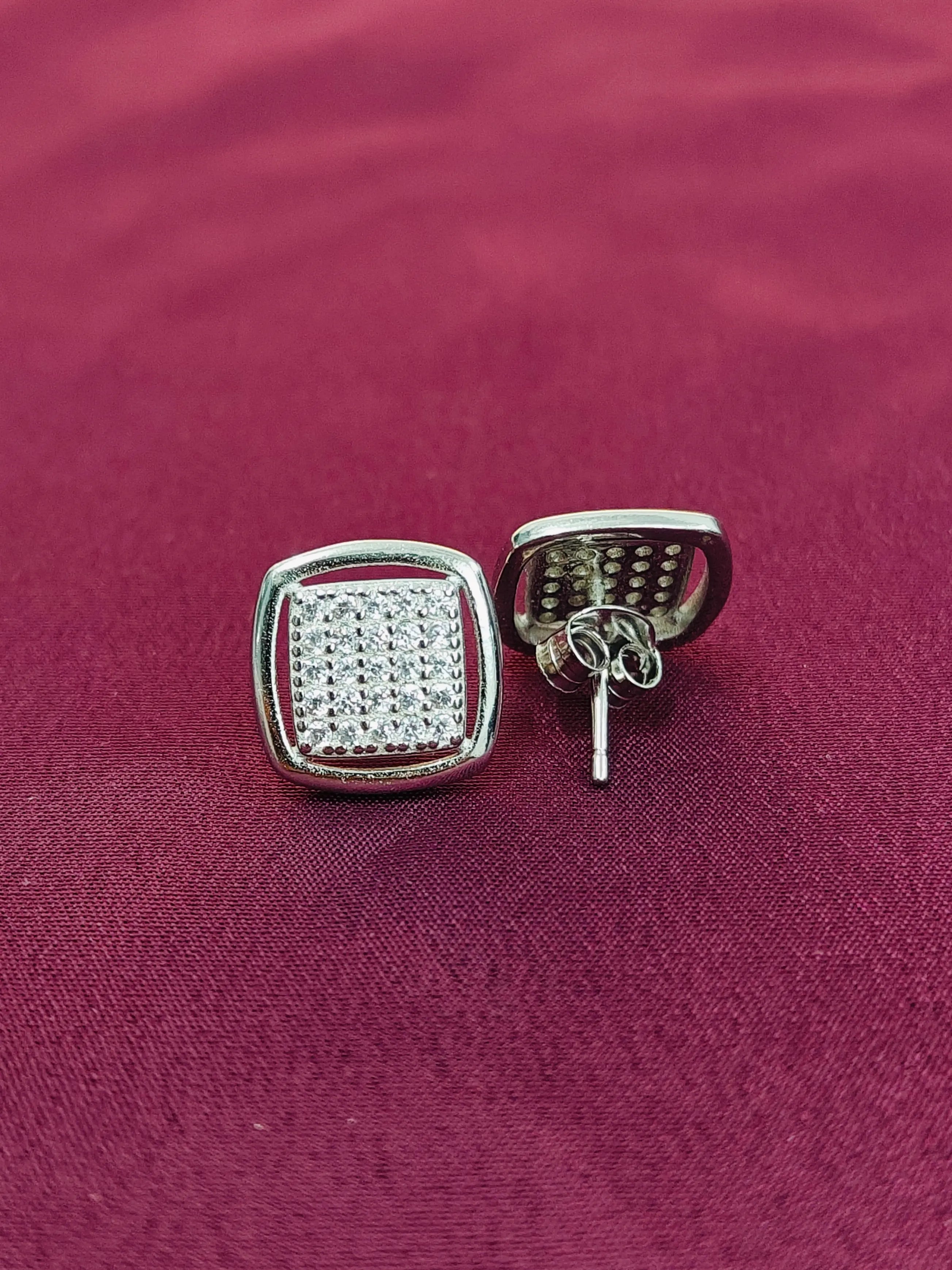 Silver square earrings with clear stones on a red fabric background